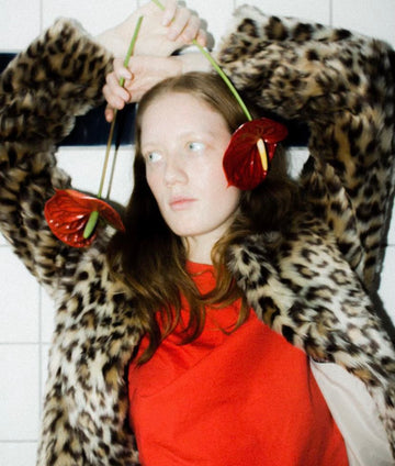 Photoshoot. A young woman holding two anthurium flowers, standing calmly and looking away, with the sculptural blooms as the focal point.